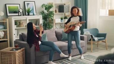可爱的非洲裔美国女人在家弹<strong>吉他</strong>, 而她的亚洲朋友则用智能手机录制视频, 微笑着享受音乐和友谊.